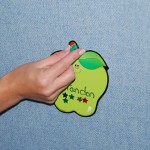 A woman's hand tacks a paper apple to a blue fabric tackable board