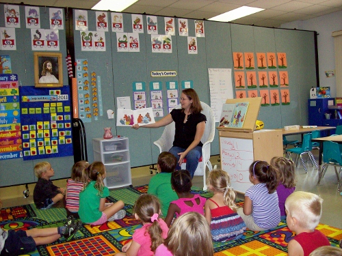 A teacher reads a book to a groups of young students