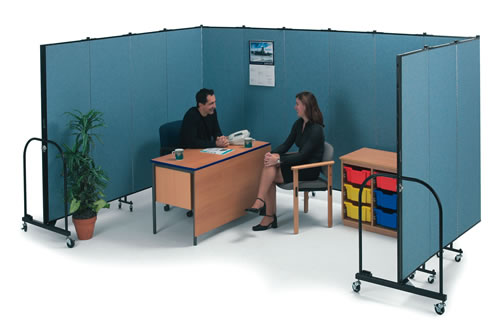 A room divider creates an office space with a man behind a desk speaking with a woman sitting in a chair on the other side of the desk