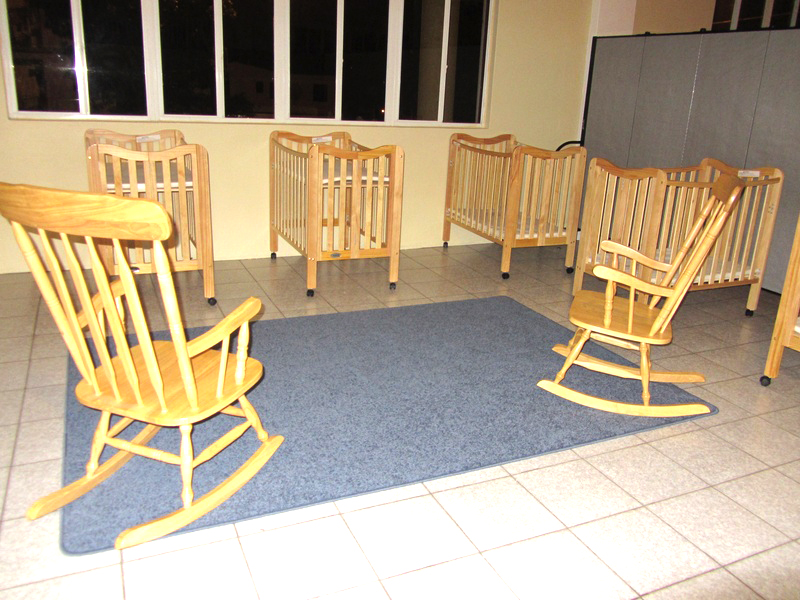 5 cribs and two rocking chairs are separated from a toddler room with room dviders