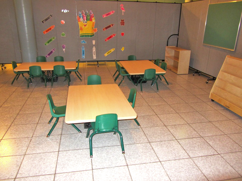 Three short tables and chairs are arranged on a tile floor in a daycare center.