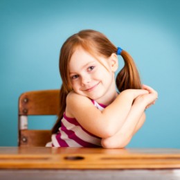 A young girl smiling while sitting at a school desk