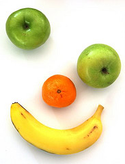 A smiley face made from a banana, an orange and two apples