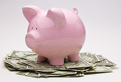 A pink piggy bank on top of a pile of dollar bills