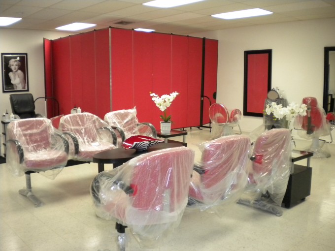 A red portable room divider with a door sections off the rear corner of a salon to create an employee workstation