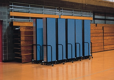 Blue Screenflex Room Dividers fodled and stored against wooden bleachers