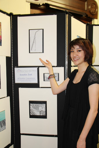 Female art student points to her charcoal drawing displayed on a Screenflex Room Divider at an art gallery.