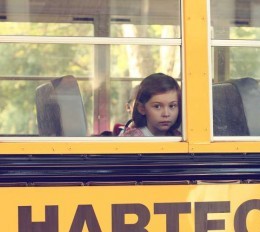 Elementary aged girl looks through a bus window as she sits by herself.