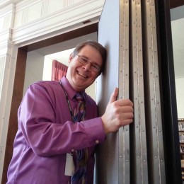 A man leans against a folded Screenflex room divider outside a library classroom.