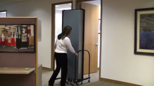 Female prepares to roll a folded Screenflex Room Divider through a standard office doorway.