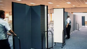 Two male workers arrange Screenflex Room Dividers into a long continuous wall in an ariport terminal.