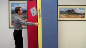 A male teacher aranges a red, yellow and blue Screenflex Display Tower.