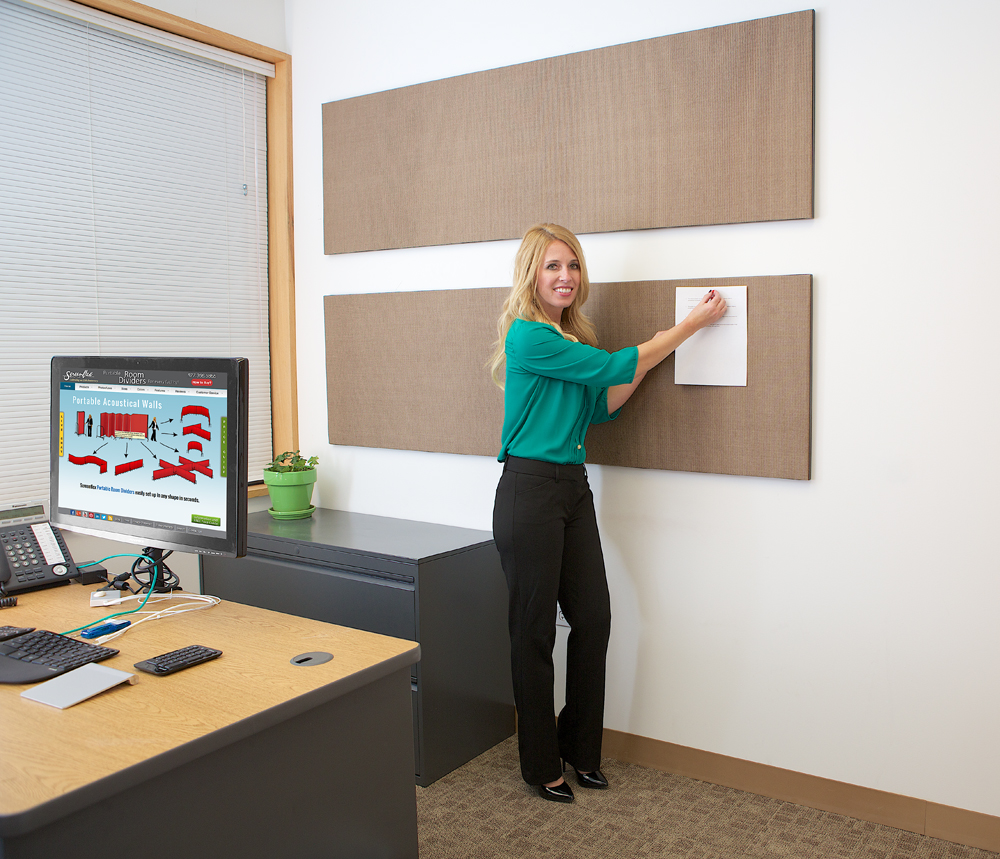 A woman tacks a piece of paper to a tackable wall panel