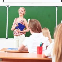new teacher stands by a chalkboard in front of students in the class.