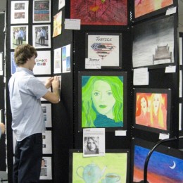 A male student tacking artwork to a tall black Screenflex Room Divider.