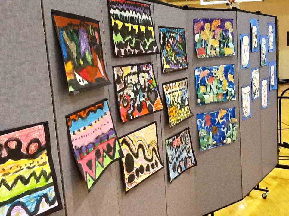 Student painted artwork displayed on Screenflex room divider with pins.