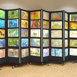 A black accordion room divider decorated with colorful children artwork
