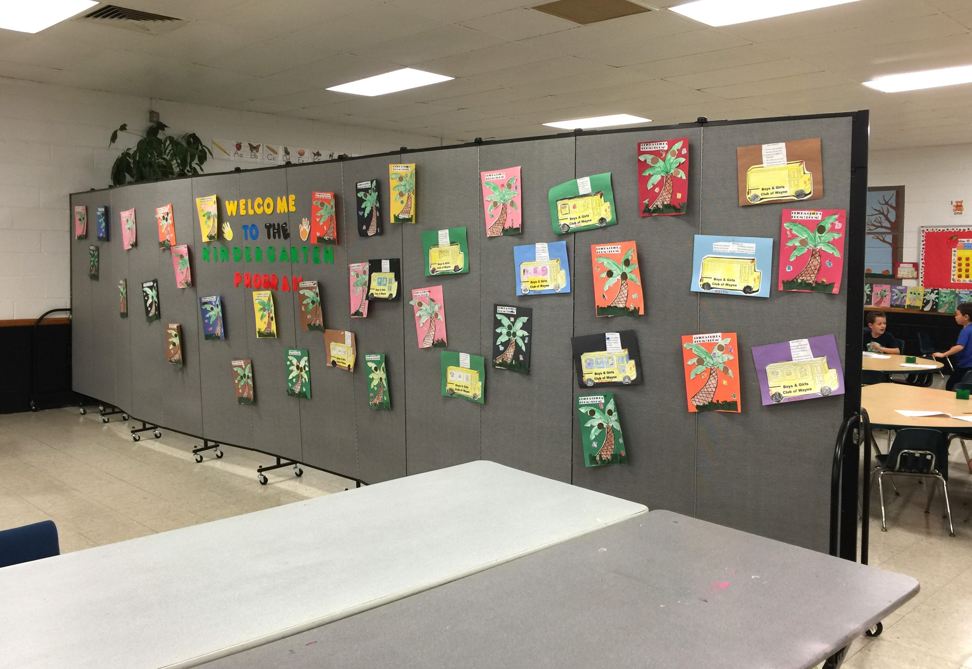 Student artwork is hung a portable wall that creates a classroom in the corner of a large room