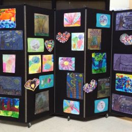 Children's artwork displayed on a black portable wall
