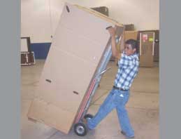 A male worker moves a large cardboard box on a metal hand truck